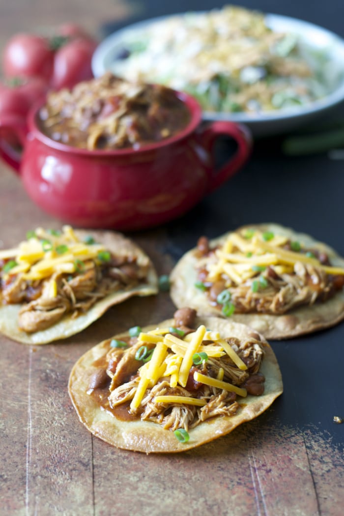 three slow cooker salsa chicken tostadas. a bowl of salsa chicken and a big salad rest in the background. 
