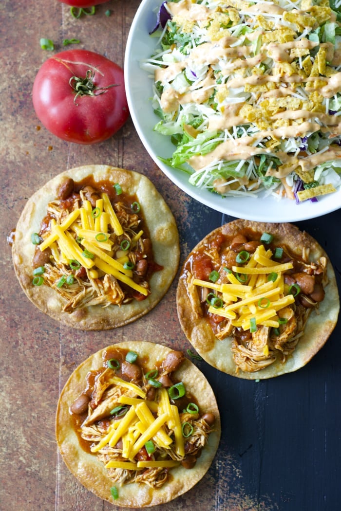 overhead view of three crockpot salsa chicken tostadas next to a big bowl of salad