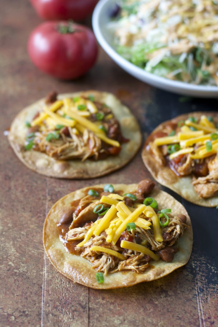 three crockpot salsa chicken tostadas next to a big bowl of salad