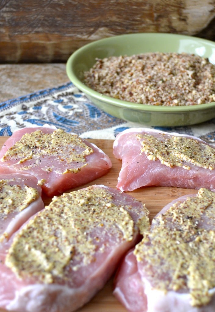 process shot showing five raw pork chops being slathered with mustard 