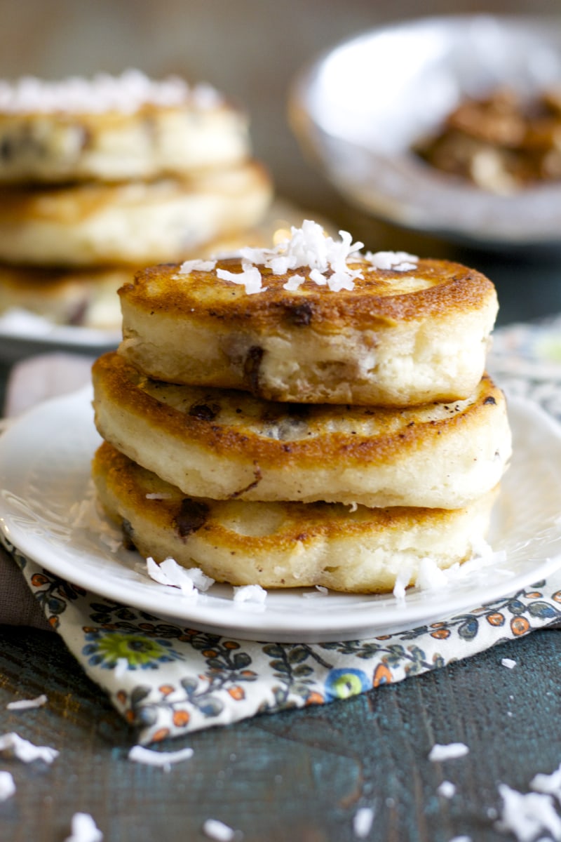 stack of three buttermilk chocolate chip pancakes on a white plate. Another stack of pancakes is in the background. 