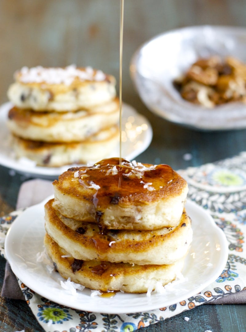 maple syrup being poured onto a stack of buttermilk chocolate chip pancakes.