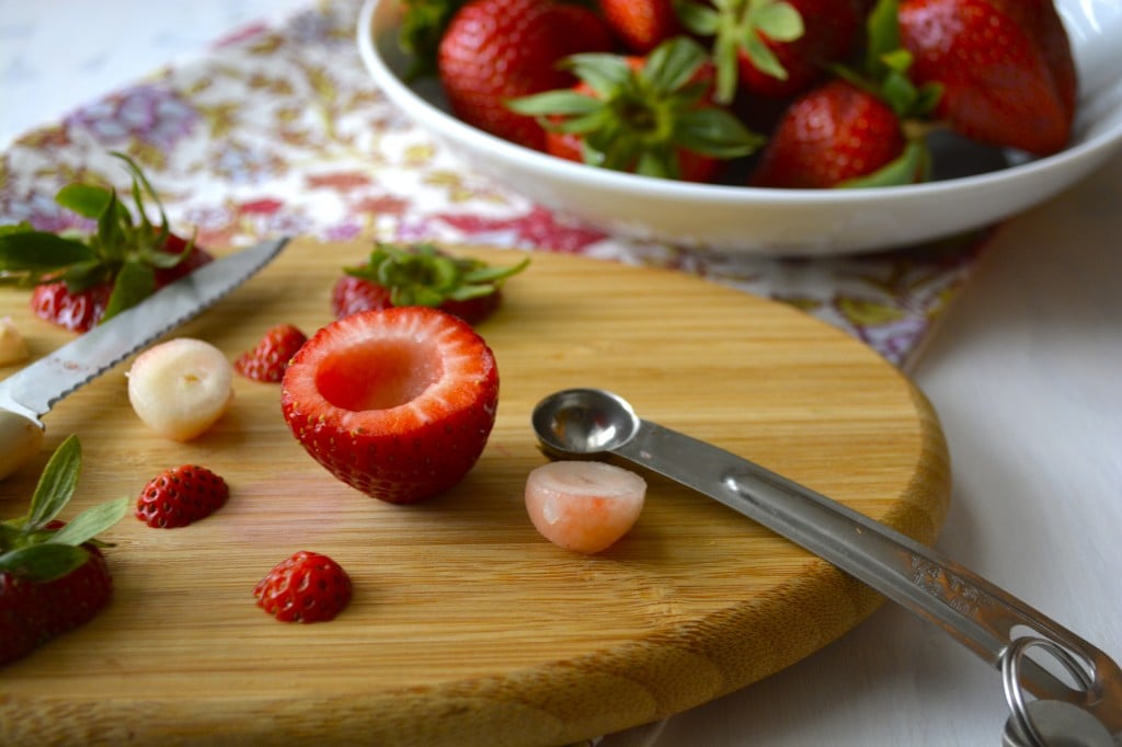 A fresh strawberry on a wood board that's been hollowed out with a small teaspoon. 