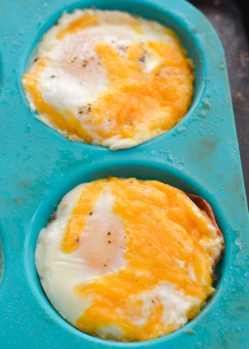Close up of baked eggs in a silicon muffin tin, topped with melted cheese