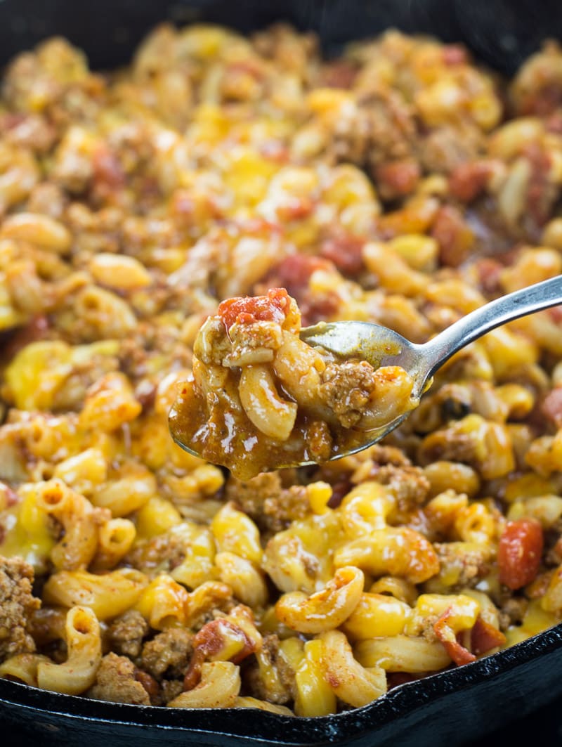 a spoonful of chili mac and cheese being held above a skillet 