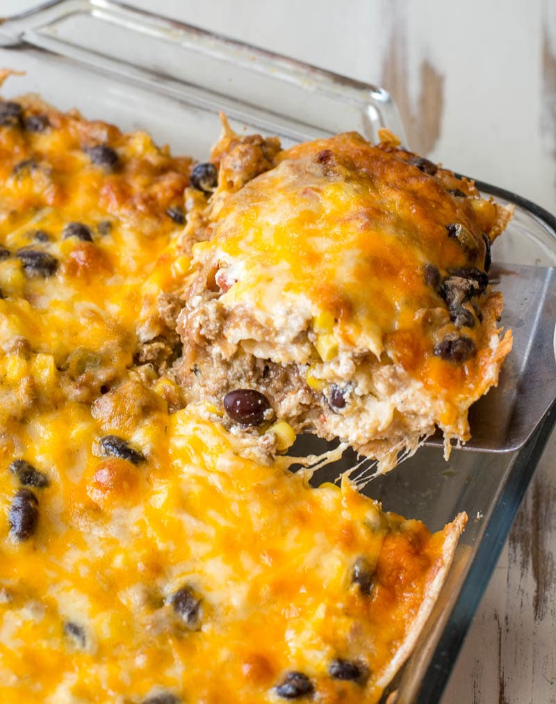 slice of taco lasagna being lifted from a baking dish 