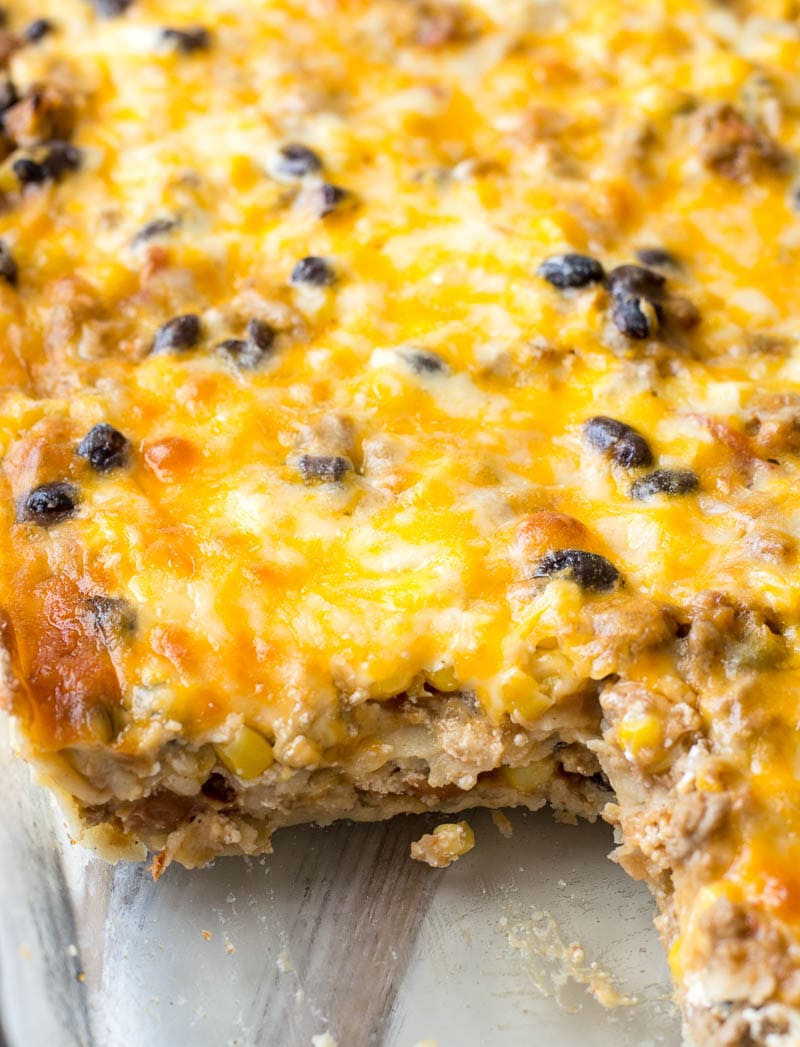 pan of taco casserole with corn tortillas with a slice missing 