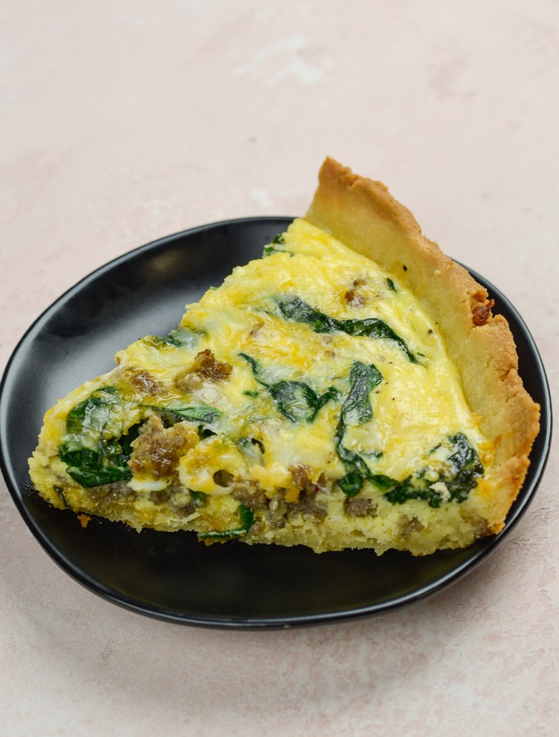 A slice of sausage spinach quiche on a dark plate 