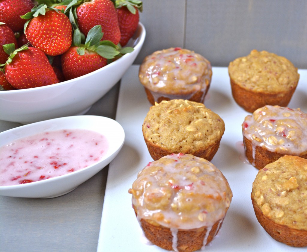six gluten free strawberry muffins on a white plate next to a dish of strawberries and glaze 