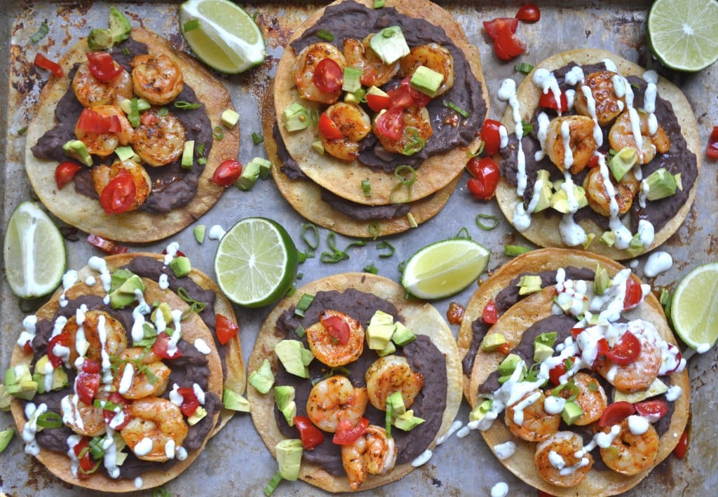 Overhead view of six homemade shrimp tostadas loaded with toppings. 