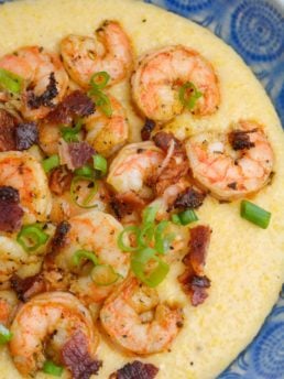 cheddar cheese grits topped with buttery shrimp, crunchy bacon, and chopped green onions in a blue bowl