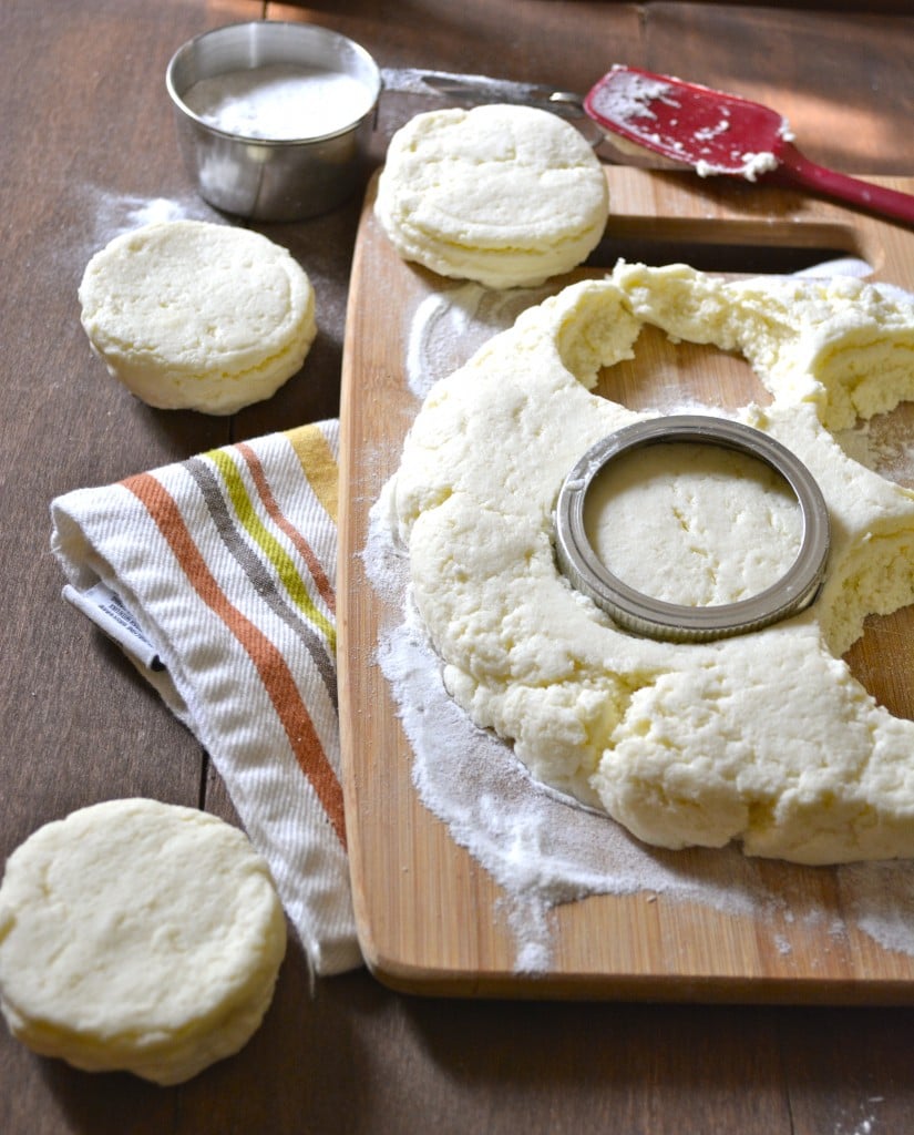 gluten free biscuit dough on a wood cutting board. A few biscuits have been punched out with a jar lid. 