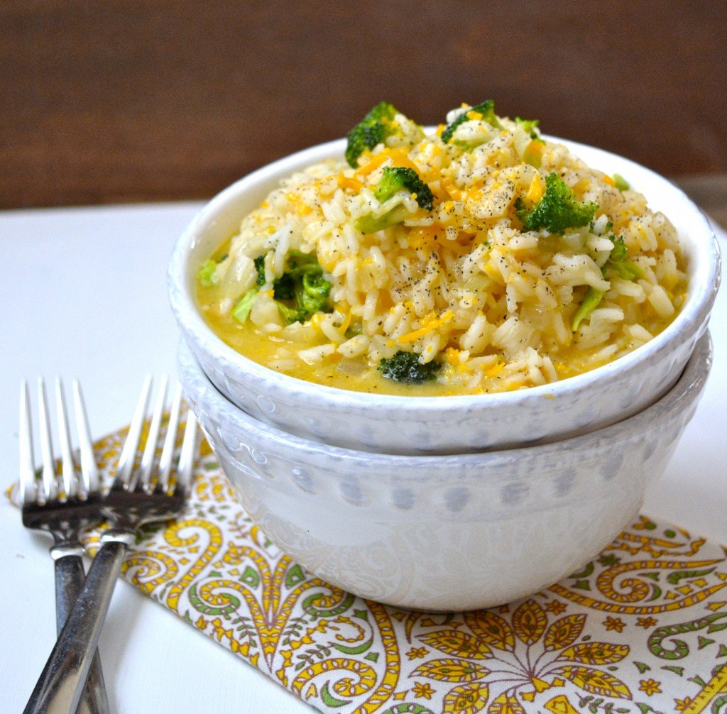 portion of broccoli and cheese rice in a white bowl. the bowl is on a napkin next to two forks 