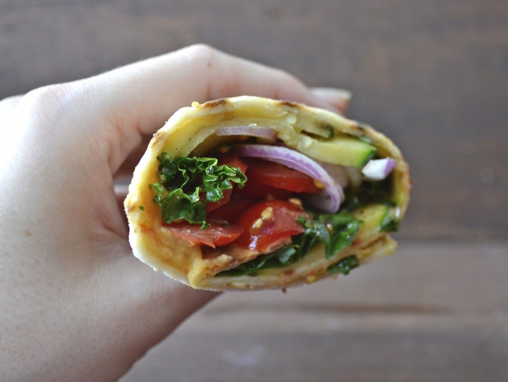 a grilled veggie and hummus wrap being held aloft, seen from the side 