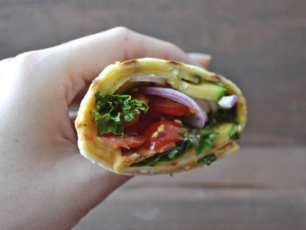 a grilled veggie and hummus wrap being held aloft, seen from the side 