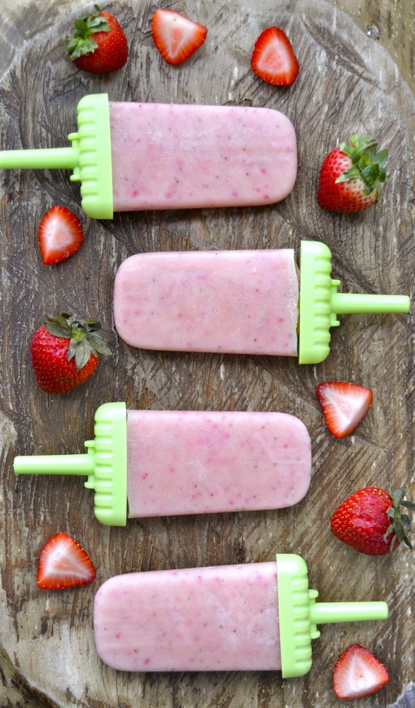 Overhead view of four strawberry pudding pops lying on their sides surrounded by sliced strawberries. 