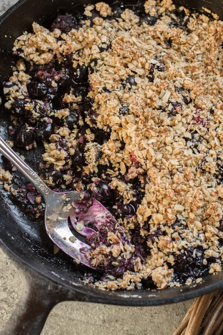 a gluten free berry crisp in a cast iron skillet. A portion has been spooned out. 