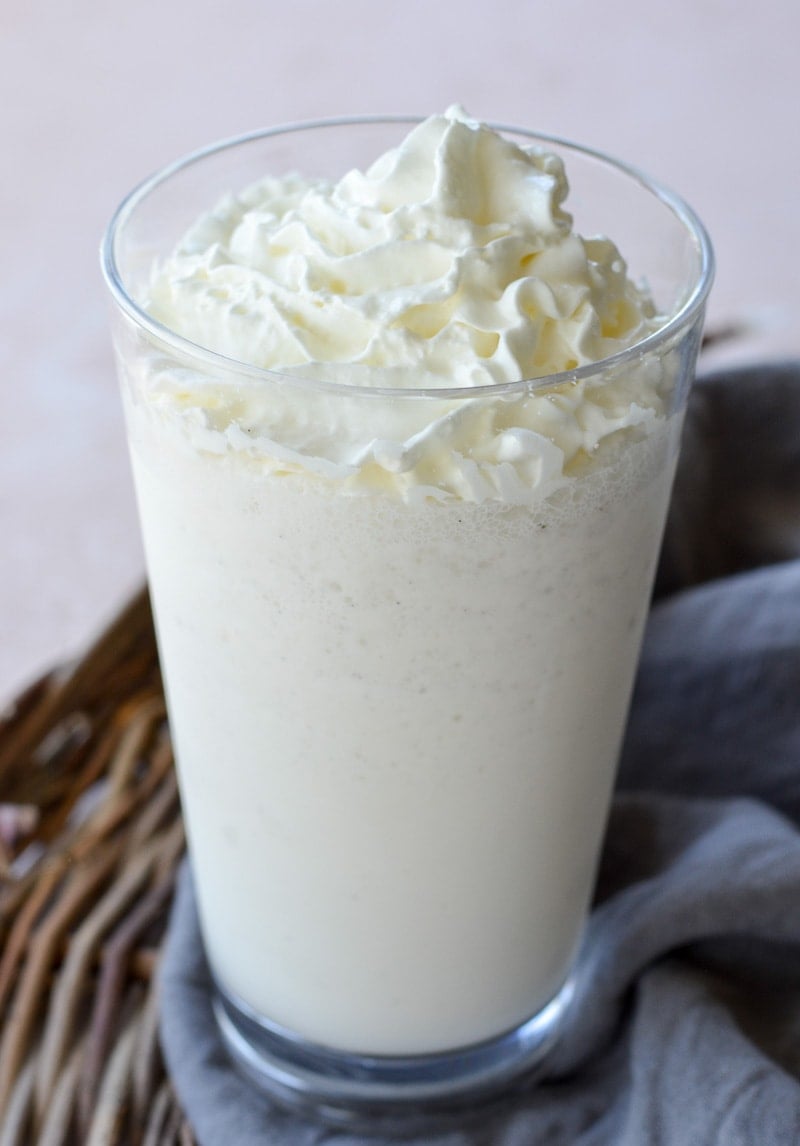 A homemade vanilla bean frappuccino in a tall glass, topped with whipped cream. 
