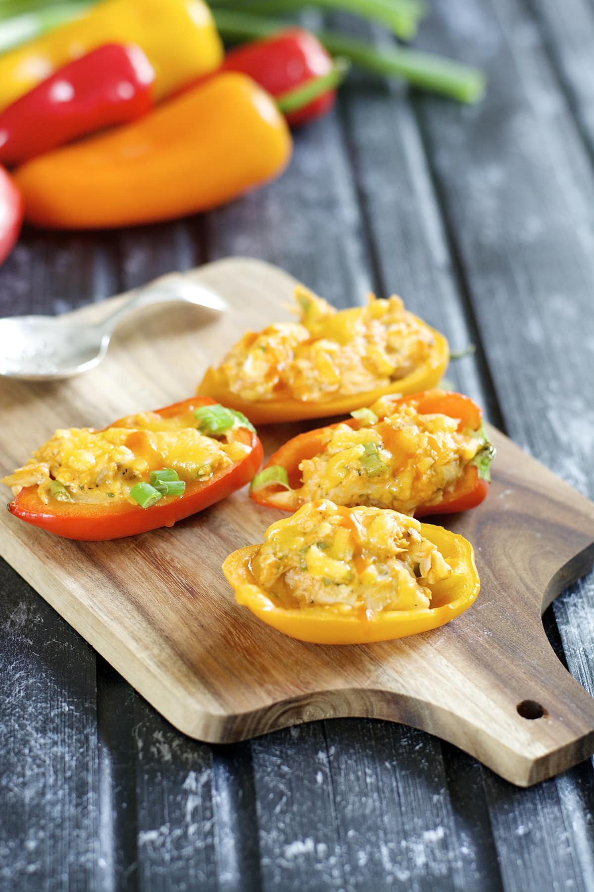 Four buffalo chicken stuffed peppers on a wood cutting board. 