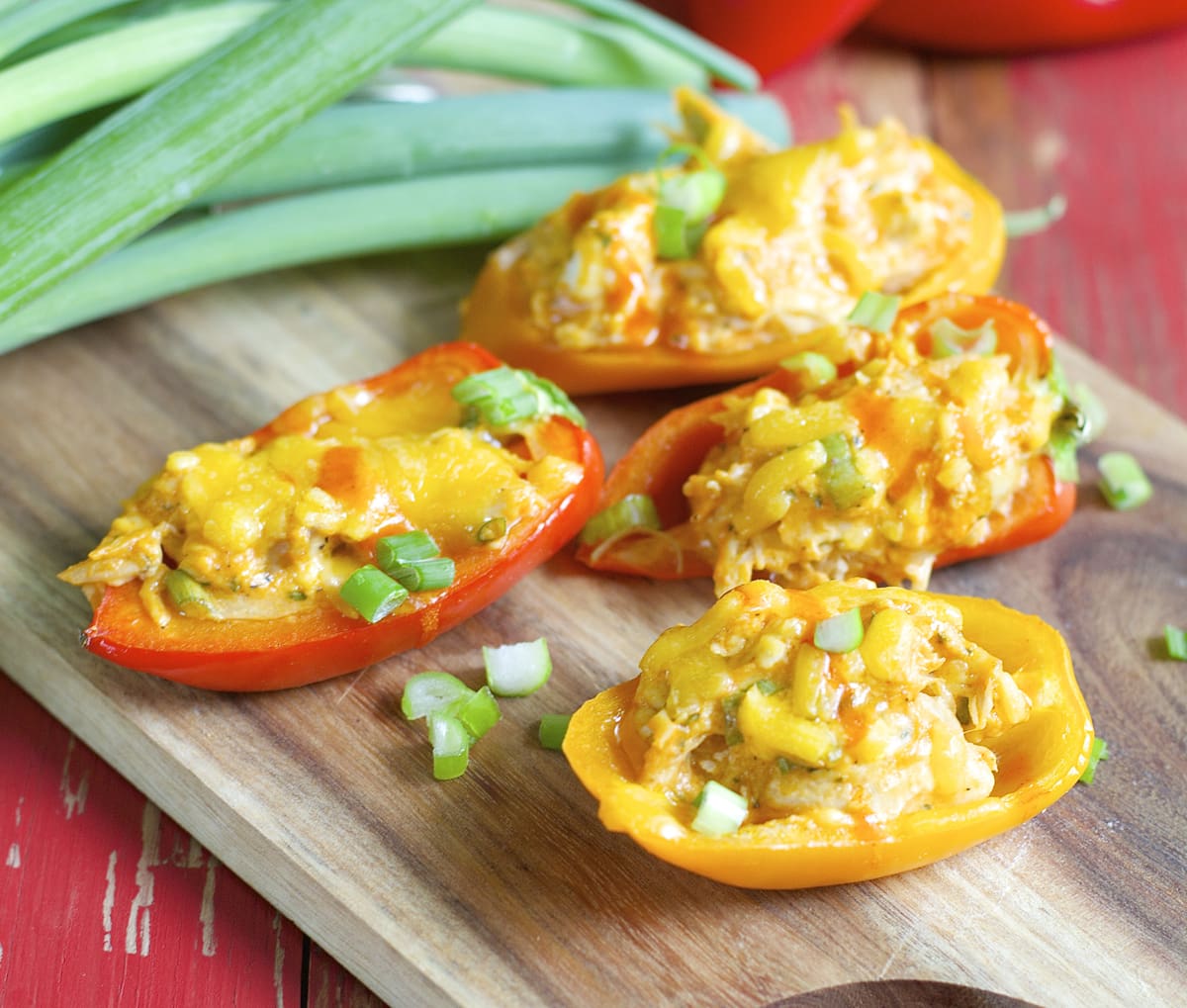 Four buffalo chicken stuffed peppers on a wood cutting board. 