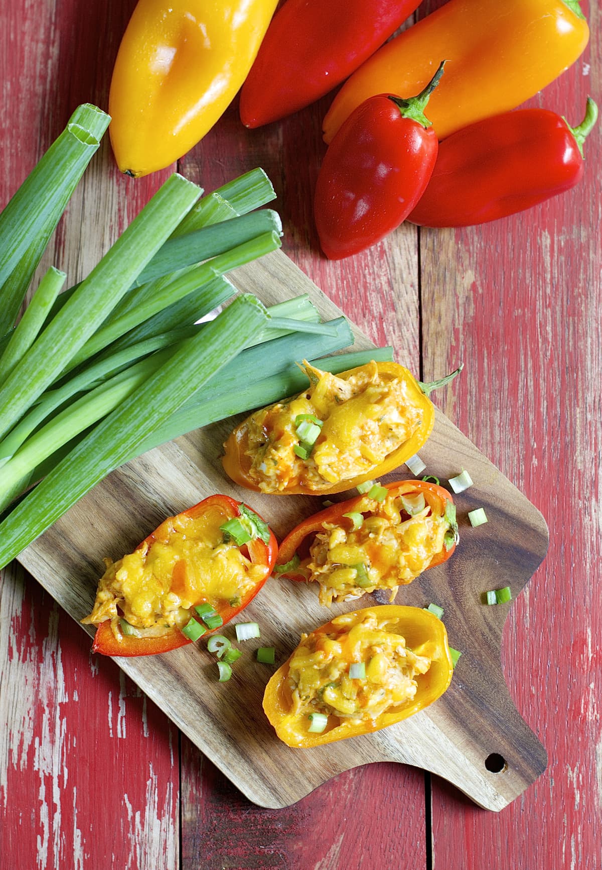 Overhead view of four stuffed sweet peppers on a cutting board next to whole sweet peppers. 