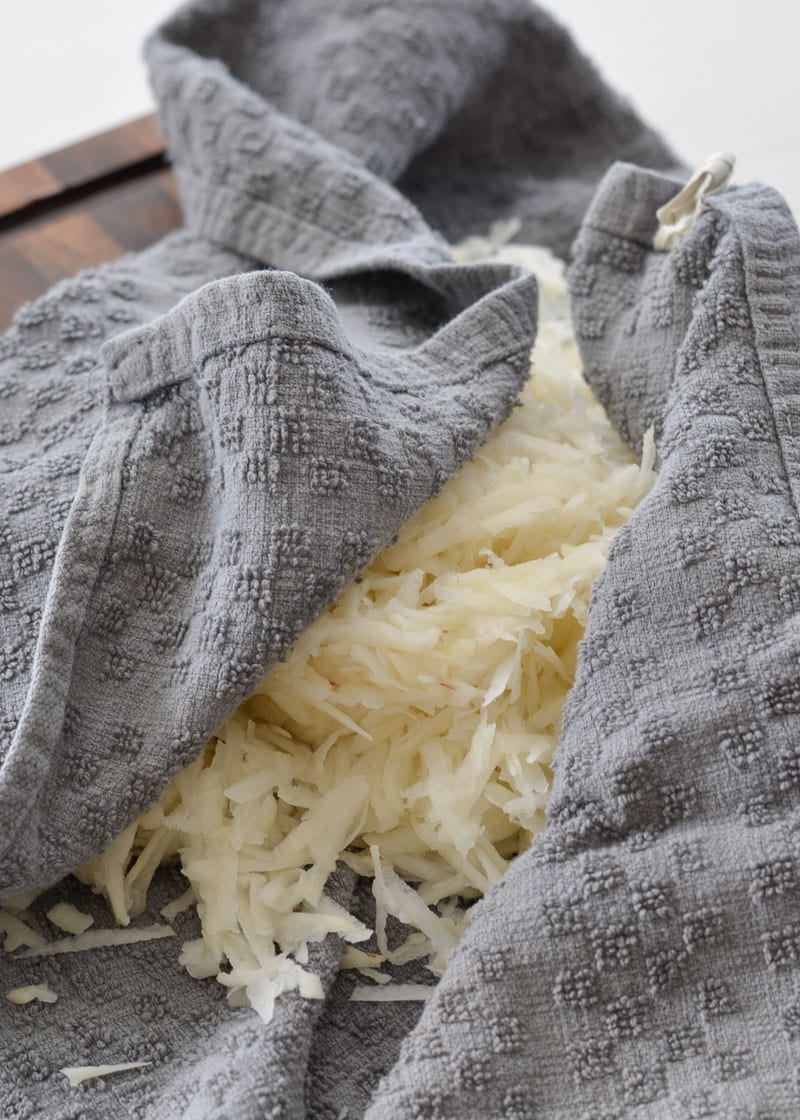 Shredded potatoes in a tea towel being squeezed.