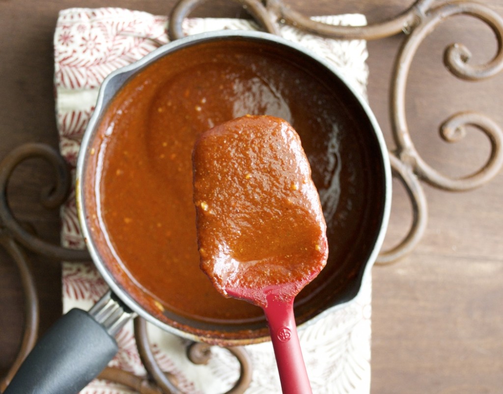 homemade red enchilada sauce in a saucepan with a spatula hovering over top