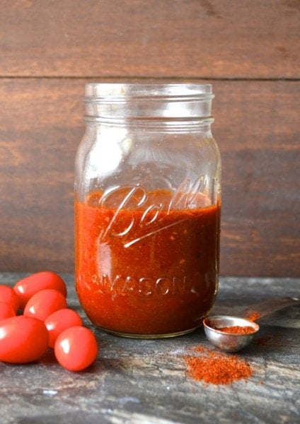 glass jar of homemade enchilada sauce with tomatoes on one side