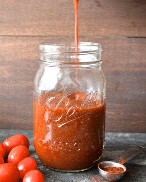 homemade enchilada sauce being drizzled into a glass ball jar