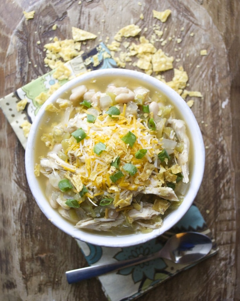overhead view of bowl of white bean chicken chili garnished with green onions, shredded cheese, and crushed tortilla chips 