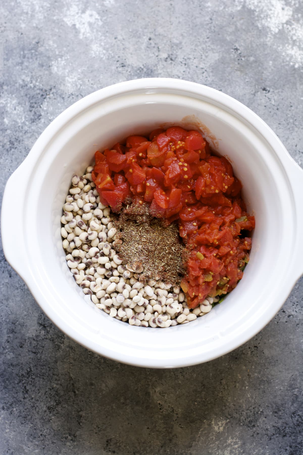 overhead view of black eyed peas, diced tomatoes and spices in a slow cooker insert 
