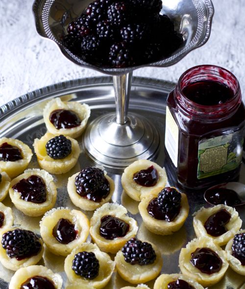 brie cheese appetizer bites on a silver tray with a jar of jam and fresh berries 