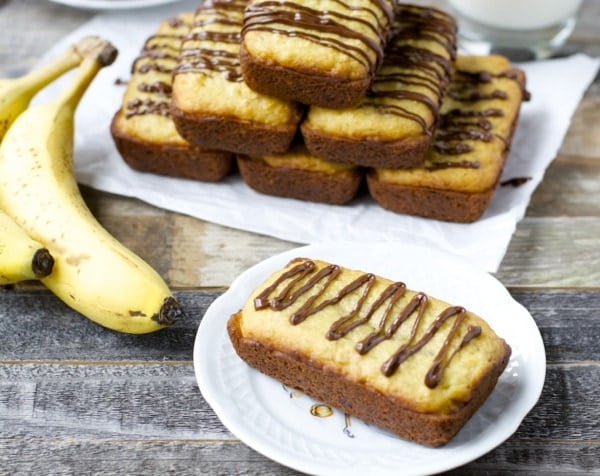 A mini loaf of gluten-free banana bread made with Bisquick. A pyramid of mini loaves and more bananas rest in the background.