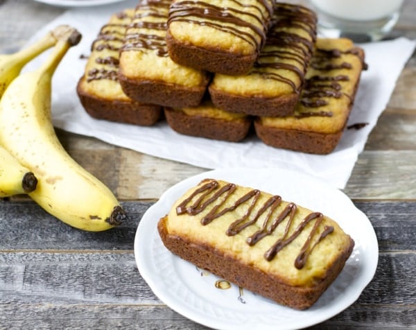 A mini loaf of gluten-free banana bread made with Bisquick. A pyramid of mini loaves and more bananas rest in the background. 