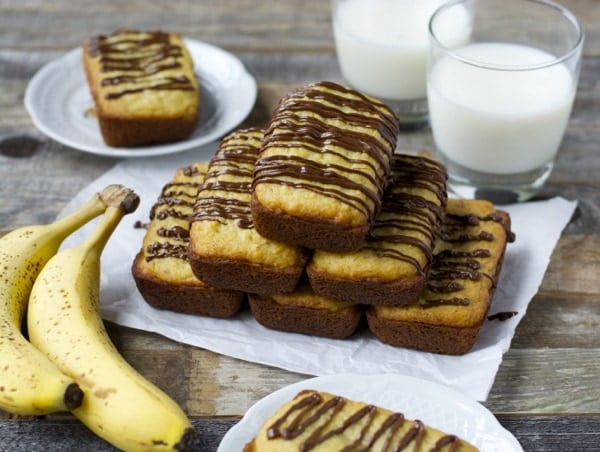 A pyramid of mini bisquick banana bread loaves drizzled with chocolate. Two glasses of milk rest in the background. 