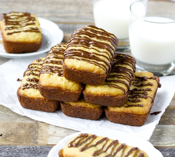 A pyramid of mini bisquick banana bread loaves drizzled with chocolate. Two glasses of milk rest in the background. 