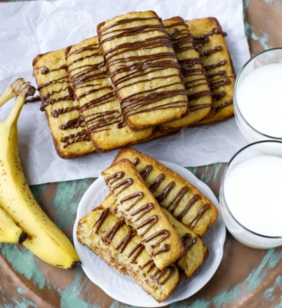 Overhead view of A pyramid of mini bisquick banana bread loaves drizzled with chocolate, two glasses or milk, and some bananas. 