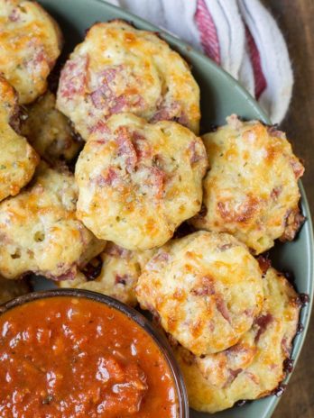 close up of multiple pepperoni pizza bites on green plate with marinara sauce