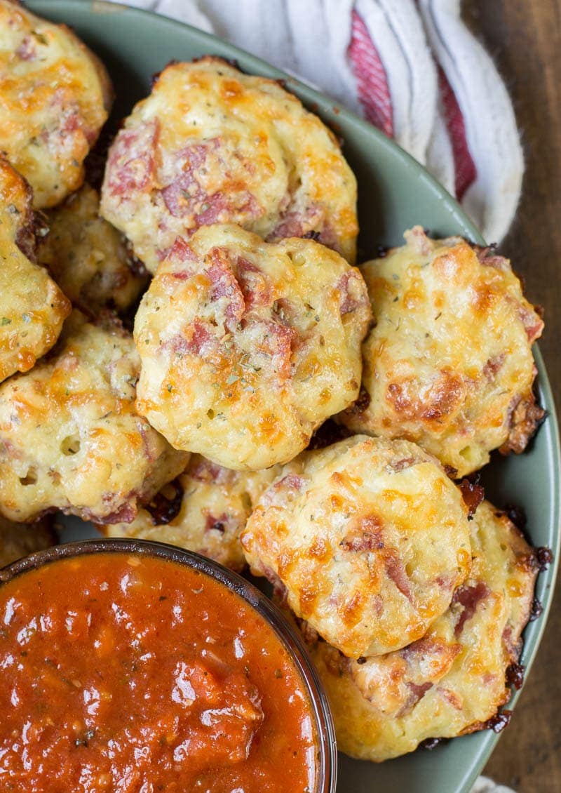 close up of multiple pepperoni pizza bites on green plate with marinara sauce