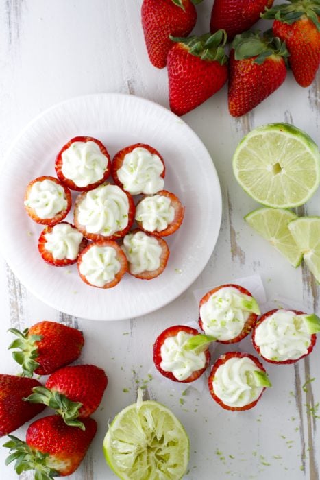 Overhead view of key lime cream cheese stuffed strawberries on a white plate. Four more are on the counter. 