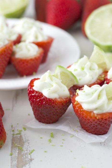 Four key lime stuffed strawberries, seen from the side. More rest on a plate in the background. 