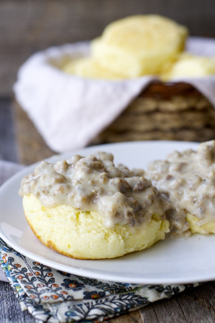 a biscuit split in half and topped with white sausage gravy on a white plate