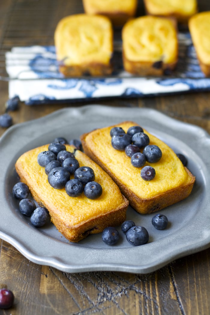 Two mini blueberry cornmeal bread loaves on a gray plate. 