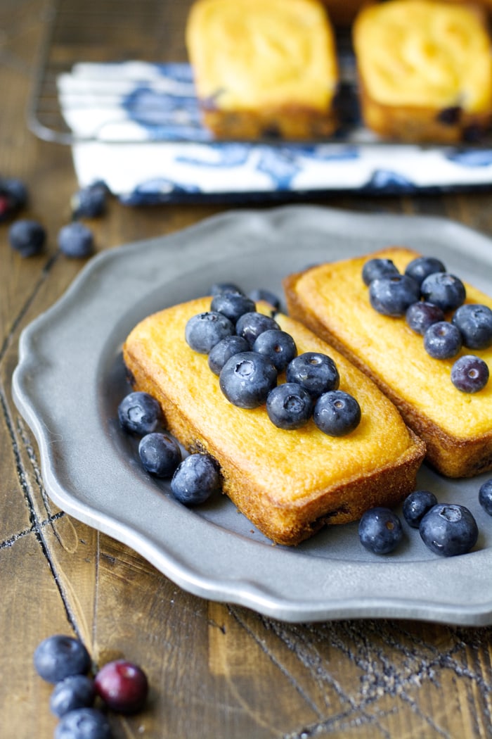 Two mini blueberry cornmeal bread loaves on a gray plate. 