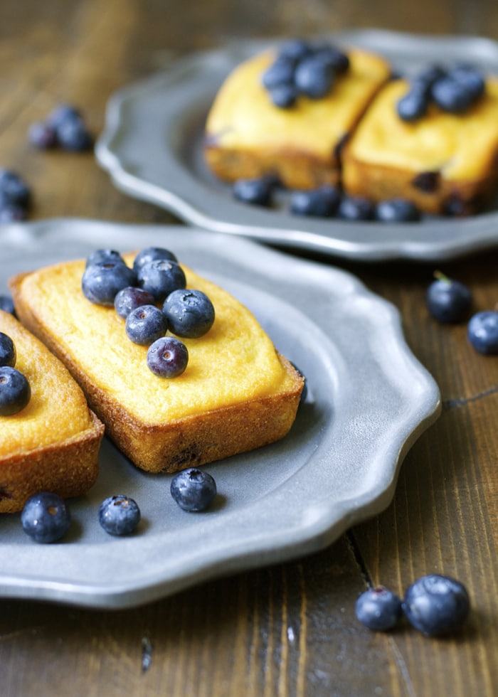 Mini blueberry cornmeal cake loaves on gray plates. 