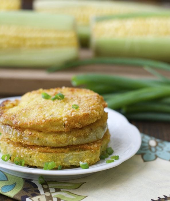 close up shot of southern fried green tomatoes on a white plate with corn in the background