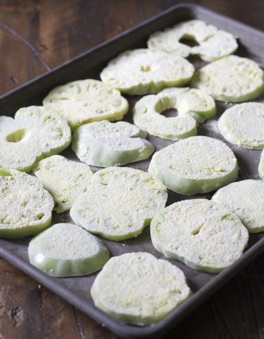 green tomato slices coated in breading on a baking tray