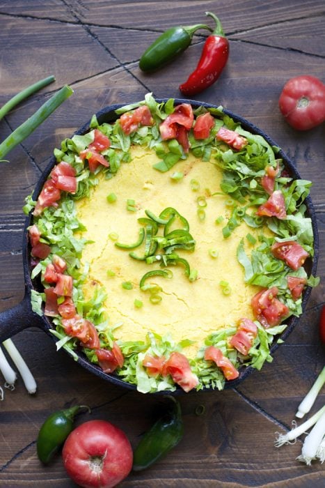 a cornbread chili pie topped with lettuce, tomato, and jalapeño slices 