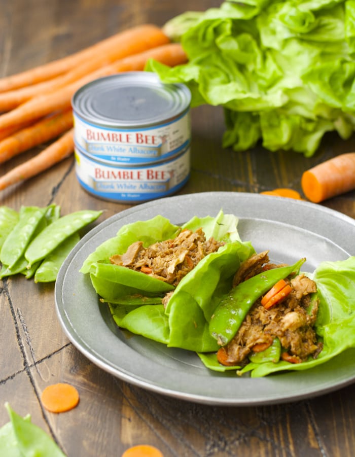 two tuna lettuce wraps on a gray plate. Cans of tuna and carrots rest in the background. 