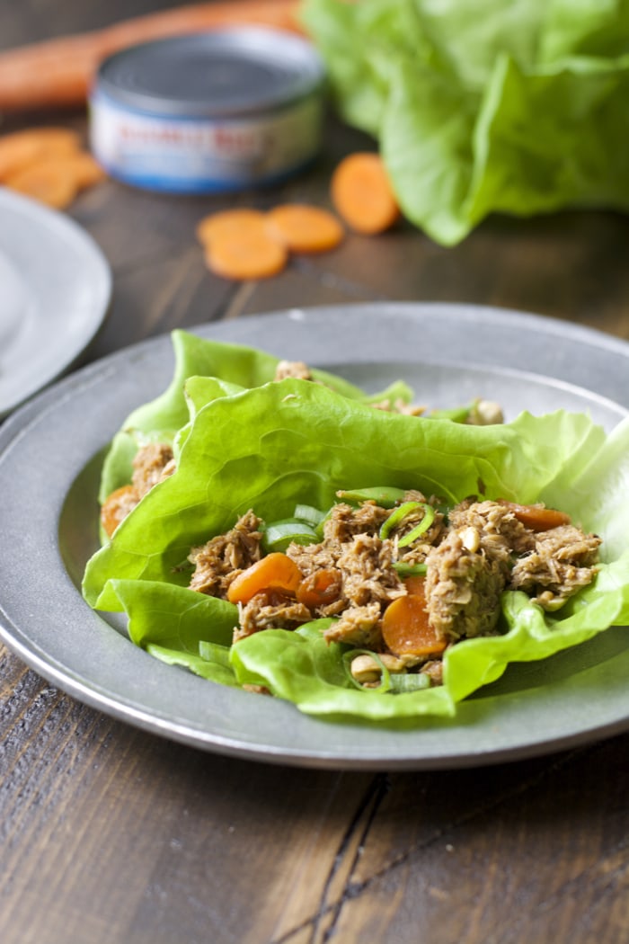 two tuna lettuce wraps on a gray plate. Cans of tuna and carrots rest in the background. 